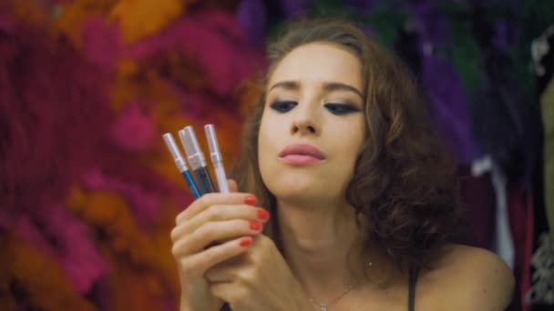 Красивая девушка делает выбор контурного карандаша для глаз перед зеркалом в раздевалке — стоковое видео