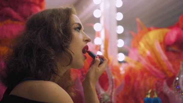 Actrice mooie jonge vrouw schildert lippen met rode lippenstift voor een spiegel, make-up in een kleedkamer — Stockvideo