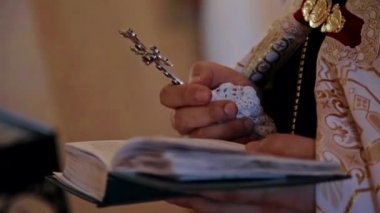 Rahip bir haç tutar ve İncil'den bir satır okur