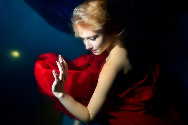 Girl in red dress dancing under water on blue background and waves. A close-up portrait. Horizontal view