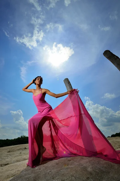 Chica afroamericana en un vestido rosa posando en una colina contra t —  Fotos de Stock