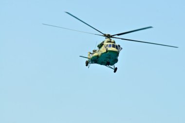 Military khaki helicopter flies against the blue sky clipart