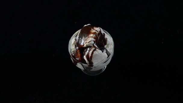 Lody z syrop czekoladowy w szklany kubek na stole obraca się na czarnym tle. — Wideo stockowe