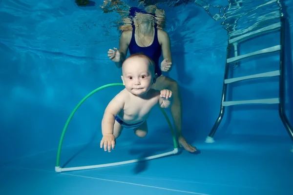 Un niño pequeño entrena en la piscina bajo el agua, nada a través del aro — Foto de Stock