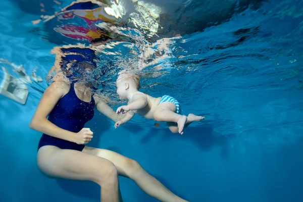 Niño aprendiendo a nadar en la piscina y nada a la madre bajo el agua — Foto de Stock