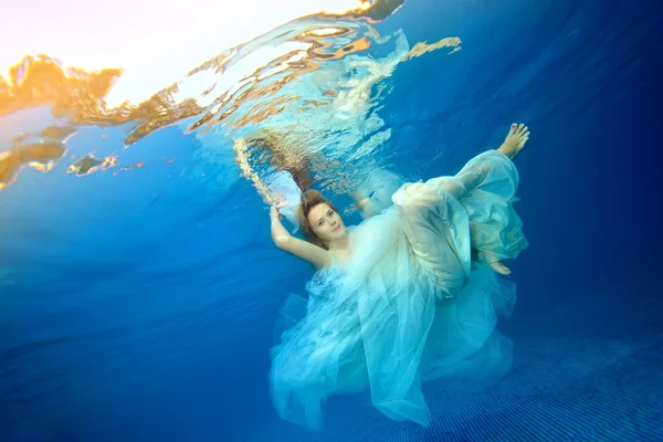 Chica bailando bajo el agua en un vestido de novia blanco sobre un fondo azul —  Fotos de Stock