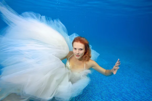 Beautiful bride in white wedding dress swims and poses underwater — Stock Photo, Image