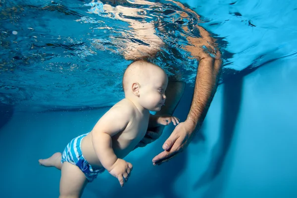 Un bebé nada bajo el agua en la piscina. Papá puso sus manos bajo el agua y atrapa al bebé. Retrato. Primer plano — Foto de Stock