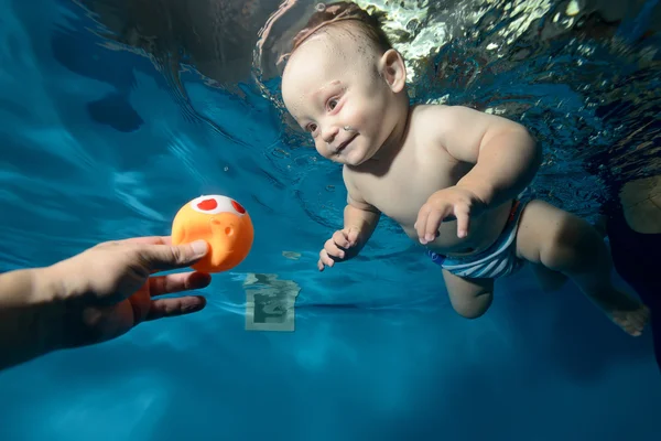 Feliz bebé nadando bajo el agua en la piscina hacia el juguete, sonriendo y riendo. Retrato. Primer plano — Foto de Stock