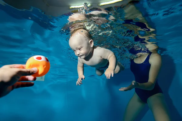Niño feliz nadando bajo el agua en la piscina hacia el juguete. Retrato — Foto de Stock