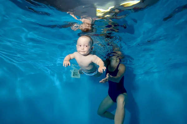 Un petit garçon flotte de ma mère sous l'eau dans la piscine sur un fond bleu — Photo