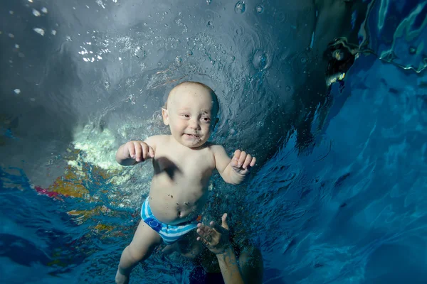 A baby swims underwater in the pool and smiling. Close-up. Portrait. Bottom view. — Stock Photo, Image