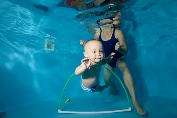 Feliz bebé entrena con su madre bajo el agua en la piscina y nadar a través del aro. Retrato. Primer plano. Orientación horizontal — Foto de Stock