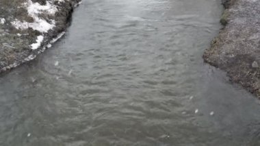 Kasvetli bir kış gününde nehrin üzerinde kar yağıyor. Suyun yüzeyine büyük kar taneleri düşer. Kötü hava. Kış manzarası. Yukarıdan manzara. 4K.