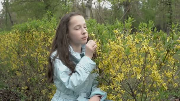 Ein junges Teenager-Mädchen mit langen Haaren schnüffelt in einem Stadtpark an gelben Blumen und blickt nachdenklich in den Himmel. Frauenporträt. Aus nächster Nähe. Konzept. 4K. — Stockvideo