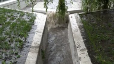 Yakın planda, şiddetli yağmur sırasında hızlı bir kirli su akıntısı taştan bir kanalizasyon oluğundan nehre akar. Kötü hava. Kavram. 4K.