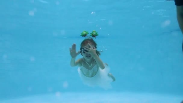 Очаровательная маленькая девочка в рождественском костюме позирует для камеры под водой в детском бассейне. Она плавает, улыбается и машет волнами. Рождество. Концепция. Портрет. Закрывай. Медленное движение. — стоковое видео