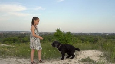 Neşeli bir çocuk, bir kız arka bahçede küçük bir köpeği eğitiyor. Köpeğe emir vermeyi öğretir ve onu yemekle cesaretlendirir. Portre. 4K.