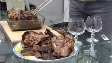 Bir adam sıcak ördek parçalarını tabağa koyar ve keser. Ön planda güzel cam bardaklar var. Durgun hayat. Kapatın. Yüzeyin derinliği. 4K