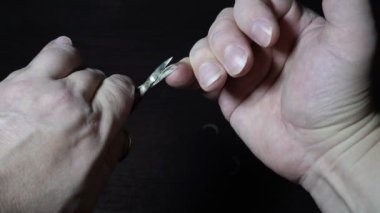 Aşırı yakın plan, bir adam siyah arka planda metal makasla sağ elinde uzun tırnaklar keser. Yukarıdan manzara. Kavram. Yüzsüz. 4K