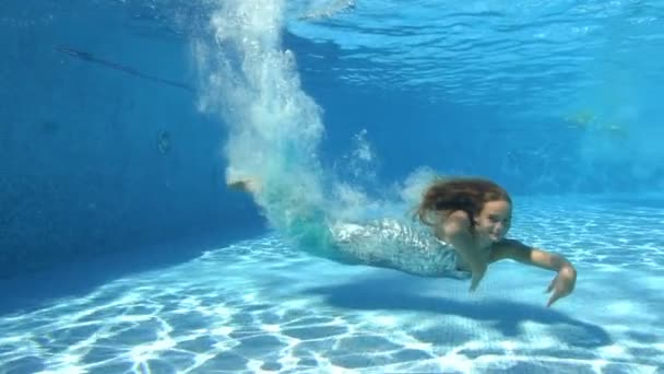긴 머리를 가진 한 아름다운 소녀는 반짝 이는 옷을 입은 채 옥외 수영장 바닥으로 잠수 한 다음, 카메라를 보고 포즈를 취하고는 서서히 수면으로 떠오른다. 크리에이티브 촬영. 초상화. 느린 동작 — 비디오
