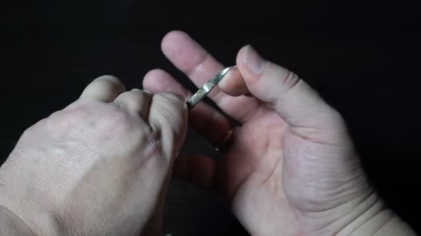 El tipo se corta sus propias uñas largas en los dedos de su mano derecha con tijeras de metal sobre un fondo negro. Primer plano extremo. La vista desde arriba. Concepto. Sin rostro. 4K — Vídeo de stock