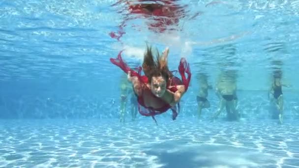 Очаровательная девушка, расслабляющая и развлекающаяся в общественном открытом бассейне. Она плавает в красном платье под водой и смотрит в камеру. Девушка с длинными волосами. Портрет. Творческая стрельба. Медленное движение — стоковое видео