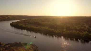 Vadinin ve nehrin üzerinden güzel bir manzara, gün batımında bir motorlu tekne hızla yol alır. Hava görüntüsü. 4K