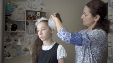 Bir anne sabahın erken saatlerinde okullu kızının kafasına beyaz fiyonk bağlar. Pencereden bakıp gülümsüyorlar. Mutlu aile kavramı. Portre. Kapatın. 4K