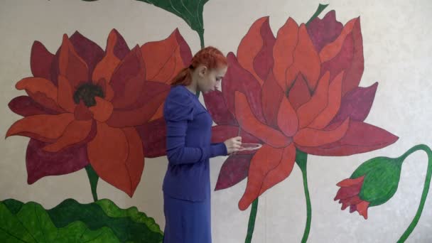 Güzel kızıl saçlı bir sanatçı kız odasındaki duvara büyük peri masalı çiçekleri çizer. Koronavirüs salgınından dolayı karantina döneminde kendini gerçekleştirme kavramı. Geniş plan. 4K — Stok video