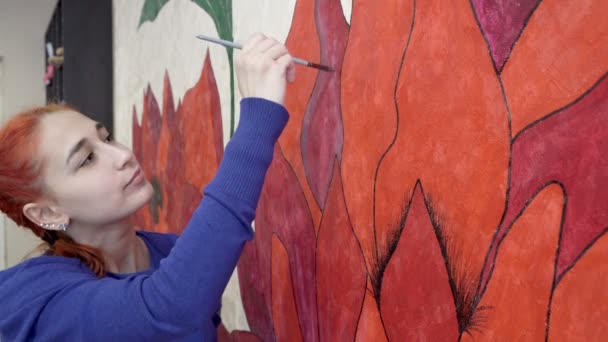 Roztomilé rusovlasé teen dívka maluje krásné červené květy na zeď v domě. Koncept tvořivosti na vlastní izolaci. Zavřít. Portrét. Soustřeď se na popředí. 4K — Stock video