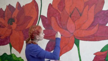Bir kız sanatçı bir webinar yönetiyor ve odasındaki duvarlara boyalar çizerek nasıl çiçek çizileceğini uzaktan öğretiyor. Mesafe öğrenme kavramı. Portre. Yakın plan. 4K
