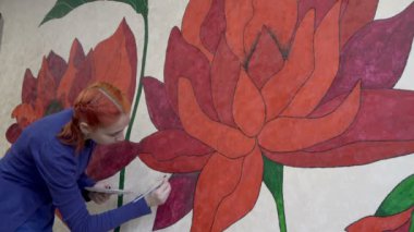 Genç bir sanatçı kız koronavirüs salgını nedeniyle karantina sırasında kendini izole ederken odasındaki duvara büyük kırmızı çiçekler çiziyor. Kavram. Portre. Yakın plan. 4K