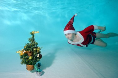 Noel Baba kostümlü küçük bir atletik çocuk havuzun dibindeki bir Noel ağacı için suyun altına dalıyor. Yüzme dersleri. Sağlıklı bir yaşam tarzı. Kutlama konsepti