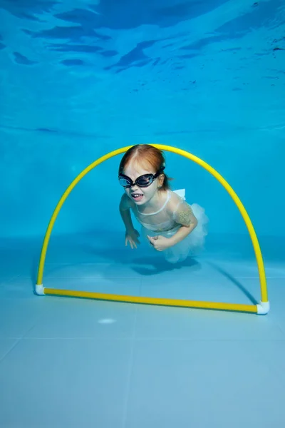 Graciosa niñita bajo el agua en la piscina infantil. El bebé nada a través del aro. Clases de natación con un niño. Estilo de vida saludable — Foto de Stock