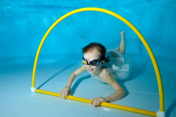 Retrato de una niña riéndose bajo el agua en una piscina infantil. El bebé nada a través del aro. Clases de natación con un niño. Estilo de vida saludable. Orientación horizontal — Foto de Stock