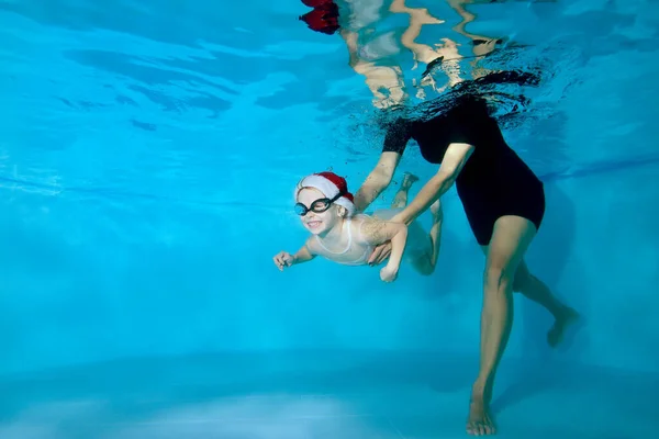 Lección con un entrenador de natación en la piscina infantil. Chica sonriente bajo el agua. Clases de natación con un niño. Estilo de vida saludable. Orientación horizontal — Foto de Stock