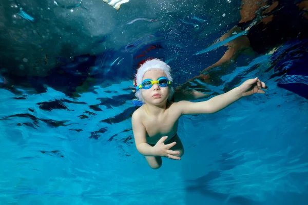 Retrato de un niño hermoso en un sombrero de Navidad y vasos en una piscina bajo el agua. El bebé aprende a bucear. Clases de natación con un niño. Estilo de vida saludable. Orientación horizontal. — Foto de Stock