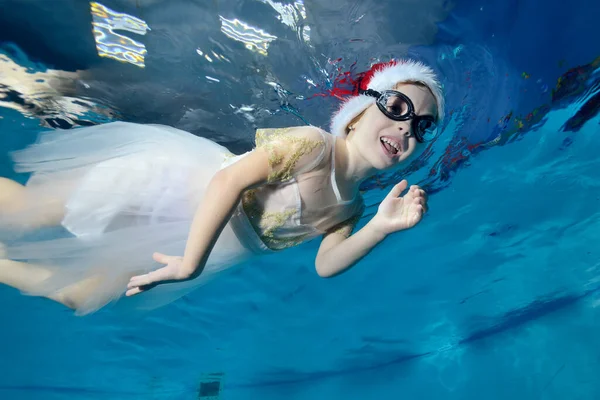 Portret van een klein meisje met een kerstmuts en een bril onder water drijvend in een kinderbad. Zwemlessen met een kind. Een gezonde levensstijl. Horizontale oriëntatie. Het concept van de viering — Stockfoto