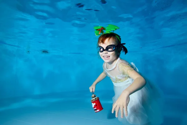 Una chica sonriente en un vestido blanco en la parte inferior de una piscina para niños con un juguete de Navidad. Decoraciones en forma de árboles de Navidad en la cabeza. Clase de natación. Orientación horizontal — Foto de Stock