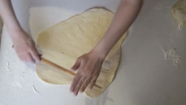Uma chef feminina estende uma fina camada de massa com um rolo de madeira na cozinha, em uma mesa branca. O conceito de cozinhar. Close-up. A vista de cima. Sem rosto. 4K — Vídeo de Stock
