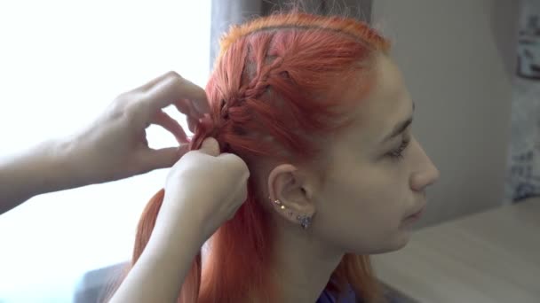 Close-up, seorang wanita mengepang kepala seorang gadis berambut merah muda yang duduk di depannya di salon kecantikan. Konsep perawatan rambut. Potret perempuan. Sisi tampilan. 4K — Stok Video