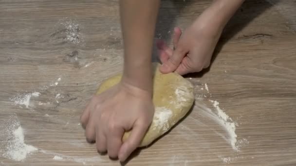 Close-up, mãos femininas amassar um pedaço de massa amarela em uma mesa de madeira. O conceito de cozinhar. A vista de cima. Sem rosto. 4K — Vídeo de Stock