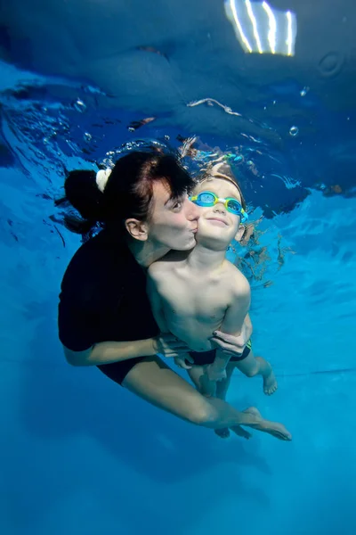 Een mooi jongetje en zijn moeder zwemmen samen onder water. Ze kust hem zachtjes op de wang. Actief gelukkig kind. Familie sportlessen. Gezonde levensstijl — Stockfoto