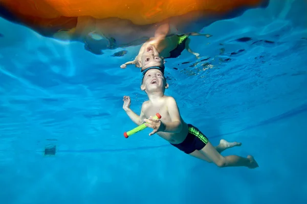 Una foto de un niño en clase bajo el agua en una piscina infantil. Nada a través del aro, saca juguetes. Niño feliz activo. Estilo de vida saludable. Clases de natación bajo el agua. Un deporte familiar — Foto de Stock