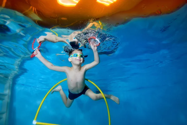 Retrato de un niño en clase bajo el agua en una piscina infantil. Nada a través del aro, saca juguetes. Niño feliz activo. Estilo de vida saludable. Clases de natación bajo el agua. Un deporte familiar — Foto de Stock