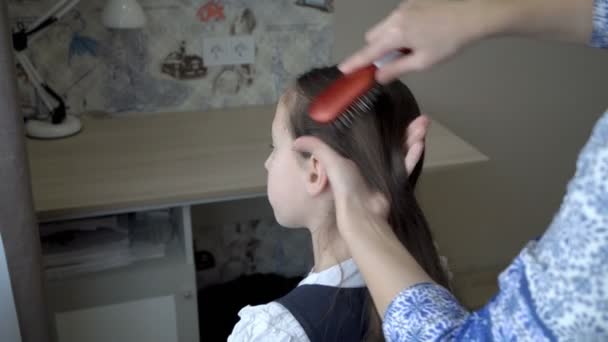 Detailní záběr, ruce dospělé ženy, která si česá vlasy malé školačky, která před ní sedí na židli časně ráno. Připravuju se do školy. Myšlenka péče. 4K — Stock video