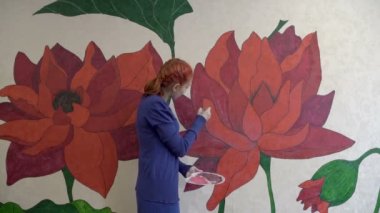 Tatlı bir kız, salgın yüzünden karantina sırasında duvardaki duvar kağıdına bir fırçayla peri çiçekleri çiziyor. Kavram. 4K