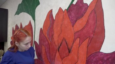 Genç bir kız yaratıcılıkla meşgul ve evin duvarına bir fırçayla güzel ve sıra dışı çiçekler çiziyor. Yaratıcılık kavramı. Yakın plan. 4K