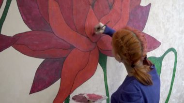 Genç bir kız, salgın yüzünden karantina sırasında duvarına kocaman bir çiçek resmi çiziyor. Odaklanma arka planda, çizimde. Konsept. Yakın plan. 4K
